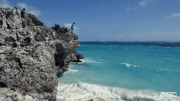 A GIF of somebody jumping off a cliff into a blue sea.